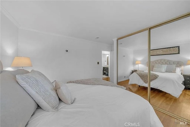 bedroom with a closet, ornamental molding, and wood finished floors