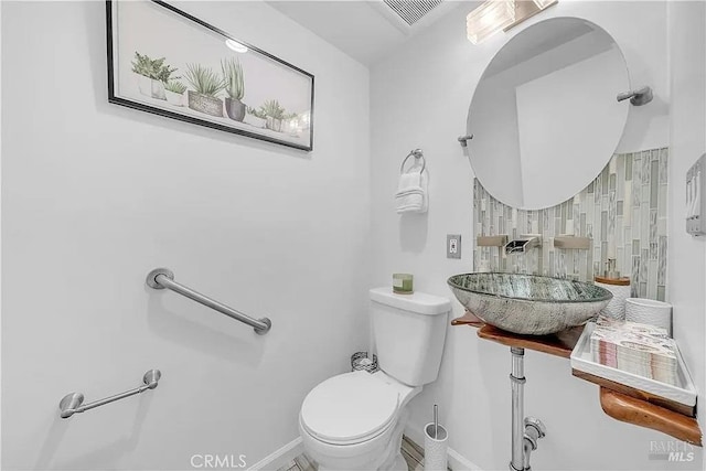half bathroom with a sink, visible vents, baseboards, and toilet