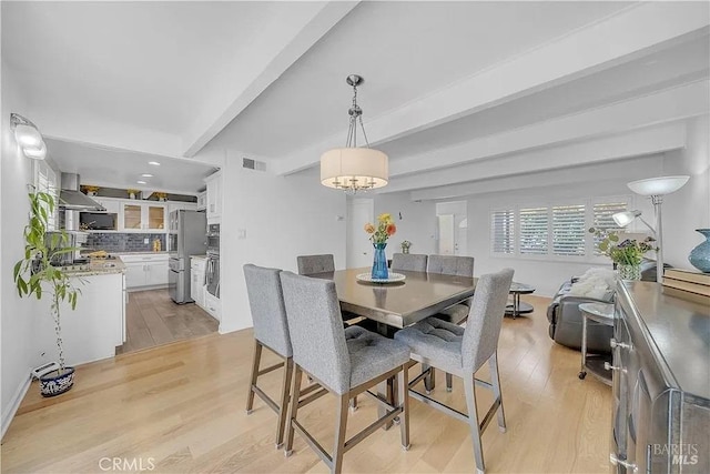 dining area featuring light wood-style floors, a notable chandelier, visible vents, and beamed ceiling