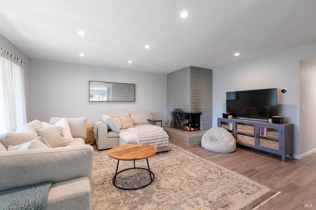 living area with a fireplace, a textured ceiling, recessed lighting, wood finished floors, and baseboards