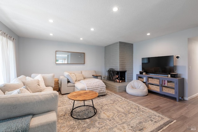 living area with a fireplace, a textured ceiling, recessed lighting, wood finished floors, and baseboards