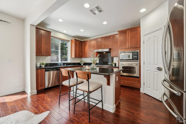 kitchen featuring visible vents, dark wood-style flooring, dark countertops, appliances with stainless steel finishes, and a breakfast bar area