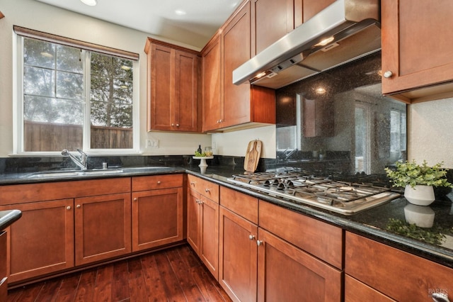 kitchen with dark stone countertops, a sink, dark wood-style floors, under cabinet range hood, and stainless steel gas cooktop