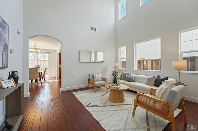 living area with baseboards, arched walkways, a notable chandelier, a high ceiling, and dark wood-style flooring