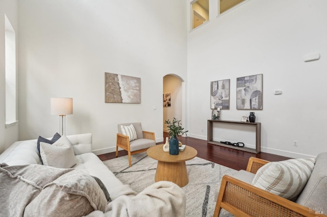 living room featuring a high ceiling, arched walkways, wood finished floors, and baseboards