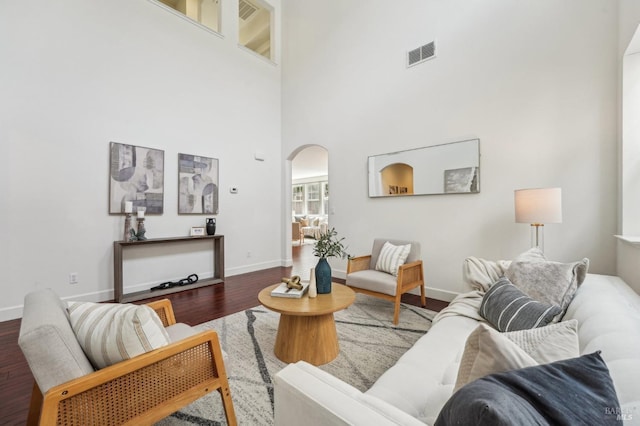 living area featuring visible vents, baseboards, arched walkways, a towering ceiling, and wood finished floors