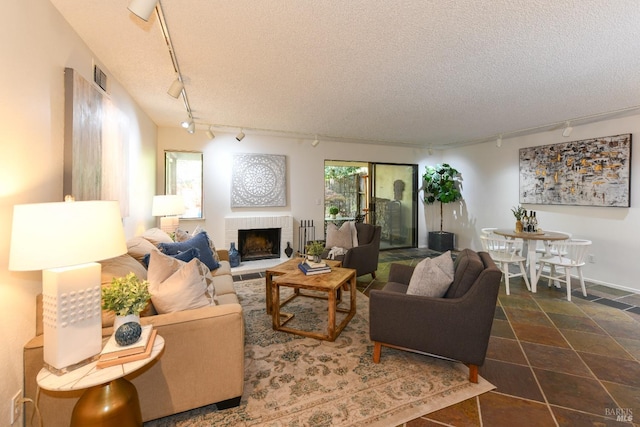 living area with a textured ceiling, visible vents, rail lighting, and a brick fireplace