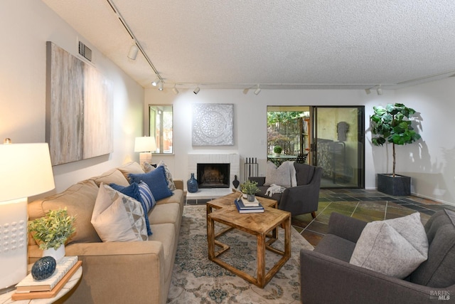 living area featuring track lighting, a textured ceiling, a fireplace, and visible vents