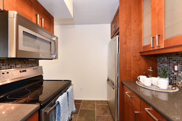 kitchen with glass insert cabinets, baseboards, appliances with stainless steel finishes, brown cabinetry, and backsplash