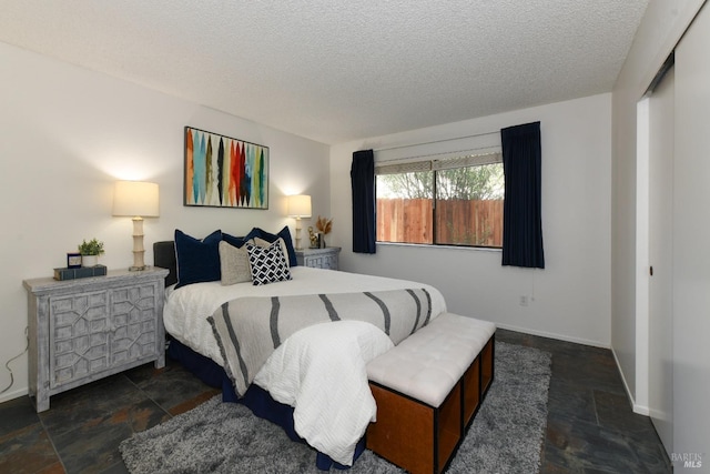bedroom featuring stone tile flooring, baseboards, and a textured ceiling