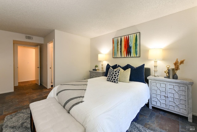 bedroom with visible vents, a textured ceiling, and stone finish flooring