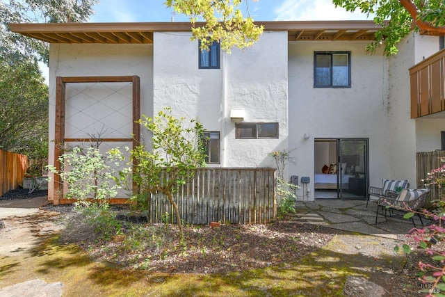rear view of house featuring a patio area, fence, and stucco siding