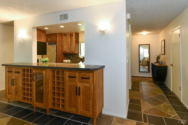 bar featuring tasteful backsplash, visible vents, baseboards, and a textured ceiling