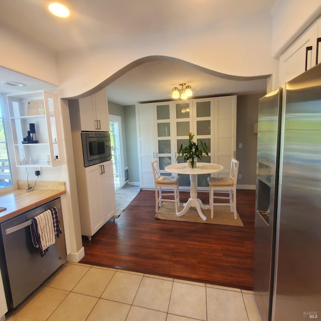 kitchen featuring baseboards, light tile patterned floors, white cabinets, appliances with stainless steel finishes, and arched walkways