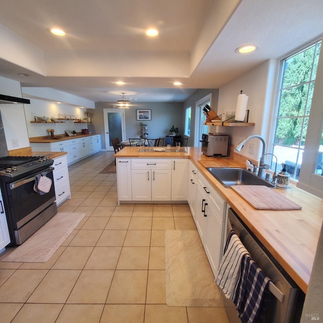 kitchen with a peninsula, white cabinets, a sink, stainless steel appliances, and wooden counters