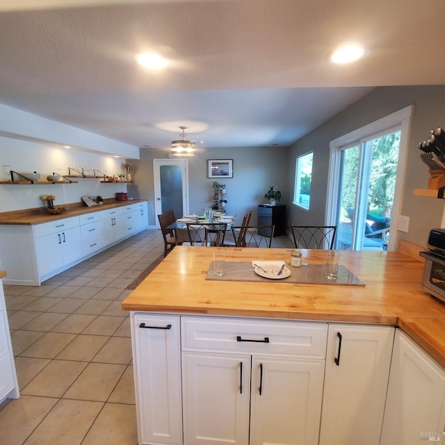 kitchen featuring wood counters, a peninsula, light tile patterned flooring, and white cabinets