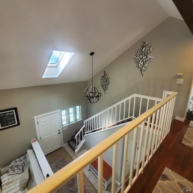 staircase featuring a chandelier, lofted ceiling with skylight, and wood finished floors