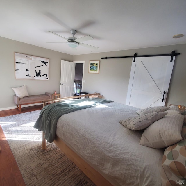 bedroom with a barn door, baseboards, a ceiling fan, and wood finished floors