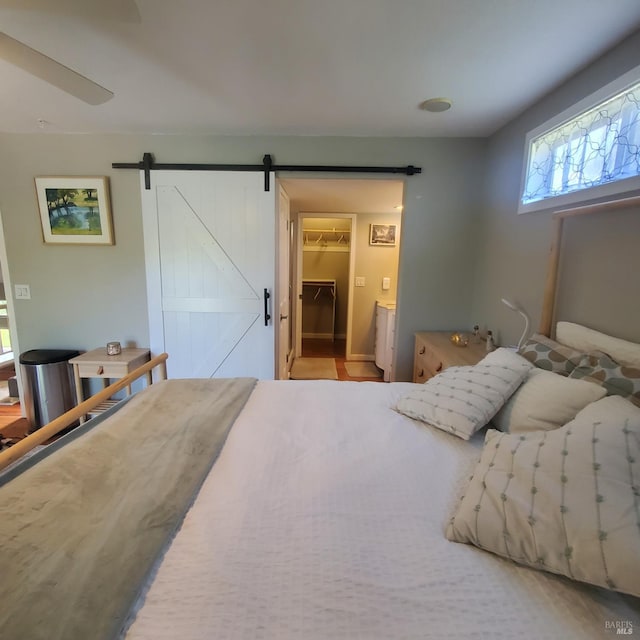 bedroom with a spacious closet, a barn door, and ceiling fan