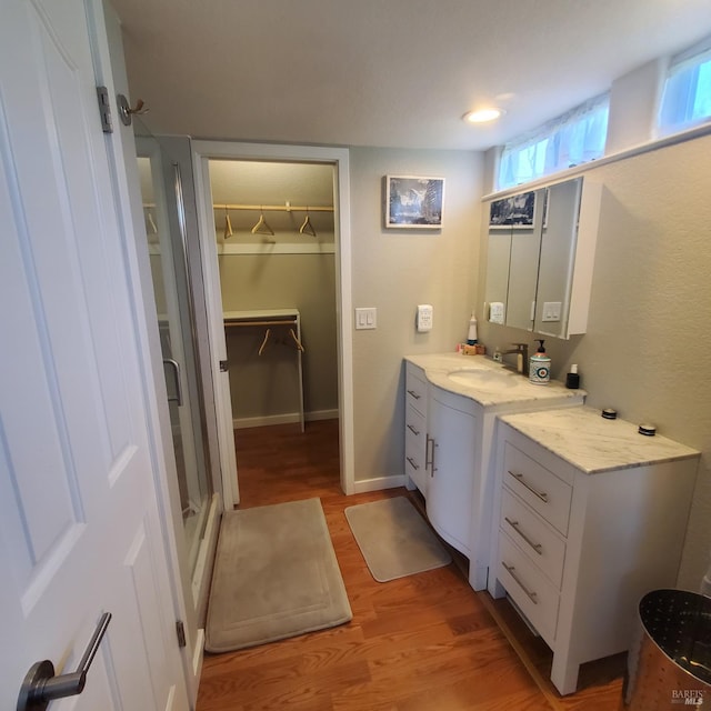 bathroom with a shower stall, wood finished floors, vanity, a walk in closet, and baseboards