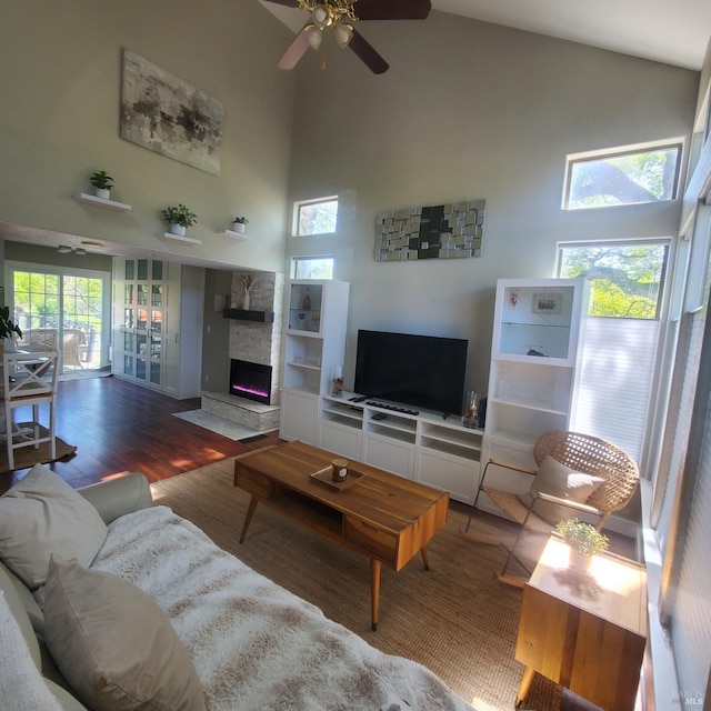 living area with high vaulted ceiling, a stone fireplace, wood finished floors, and ceiling fan