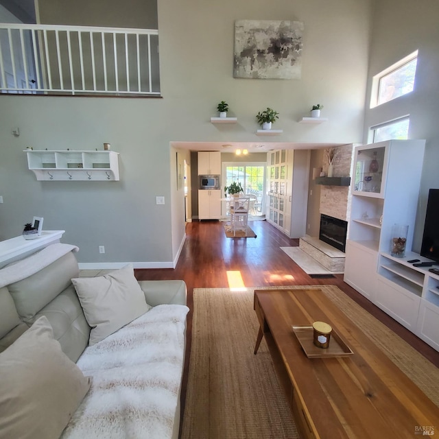 living area with a high ceiling, wood finished floors, baseboards, and a stone fireplace