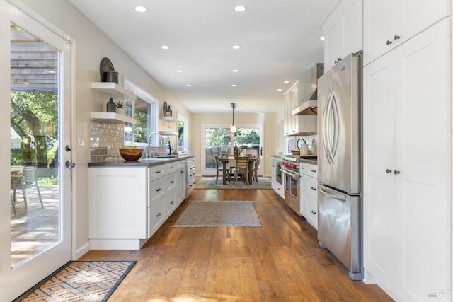 kitchen with white cabinets, wall chimney exhaust hood, hardwood / wood-style floors, stainless steel appliances, and a sink