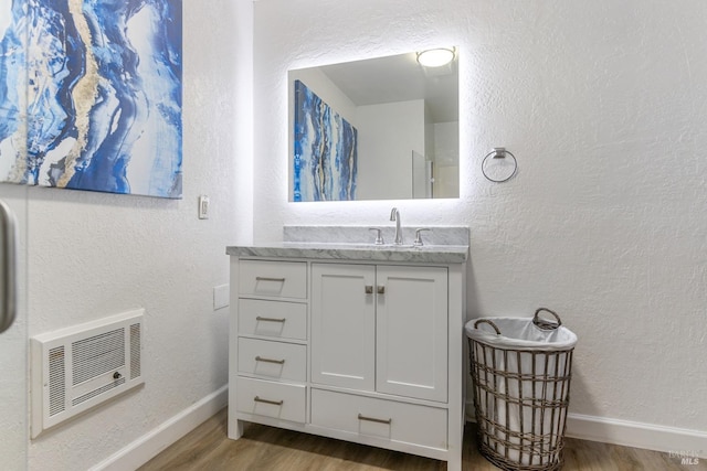 bathroom with wood finished floors, vanity, baseboards, and heating unit