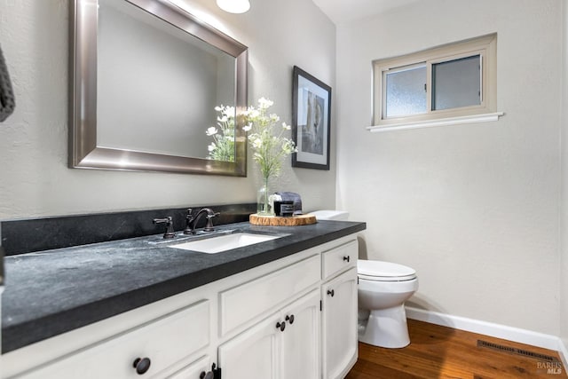 half bath with vanity, visible vents, toilet, wood finished floors, and baseboards