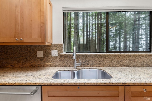 interior details with tasteful backsplash, light brown cabinetry, light stone counters, dishwasher, and a sink