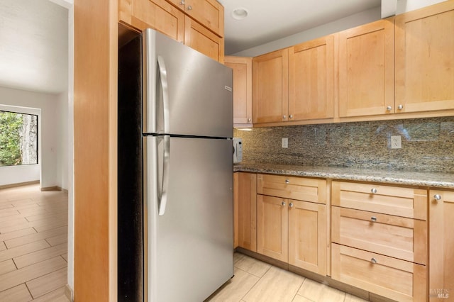 kitchen with baseboards, light brown cabinets, freestanding refrigerator, light stone countertops, and decorative backsplash