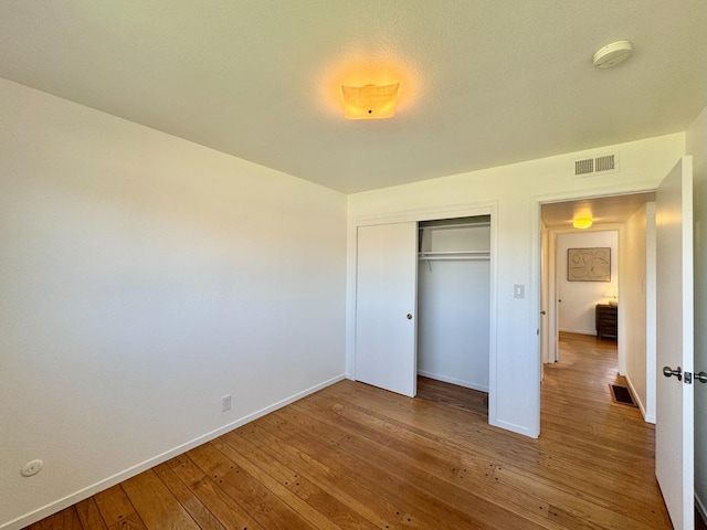 unfurnished bedroom featuring visible vents, a closet, hardwood / wood-style flooring, and baseboards