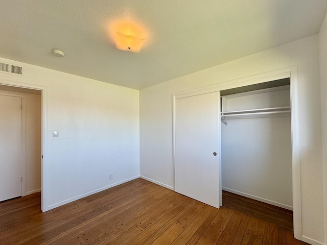 unfurnished bedroom featuring visible vents, a closet, baseboards, and wood-type flooring