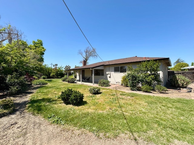 rear view of house featuring a yard, stucco siding, a chimney, and fence