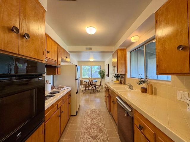 kitchen featuring white appliances, under cabinet range hood, tile counters, brown cabinets, and a sink