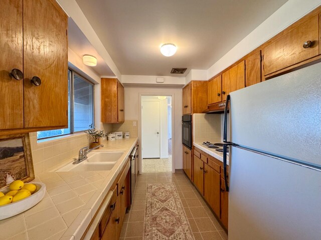 kitchen featuring brown cabinets, a sink, tile counters, backsplash, and white appliances