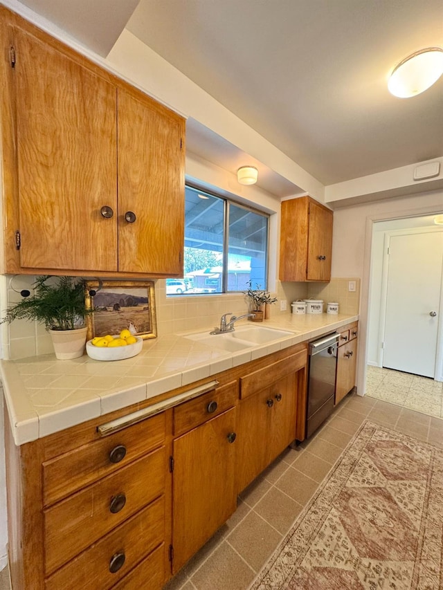 kitchen with brown cabinetry, dishwasher, decorative backsplash, and a sink