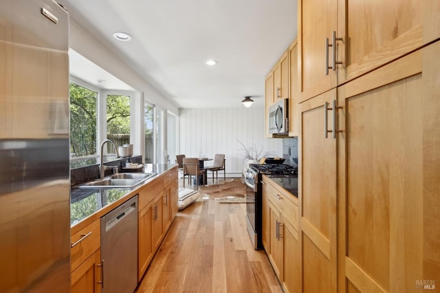 kitchen with light wood-type flooring, recessed lighting, dark countertops, a sink, and stainless steel appliances