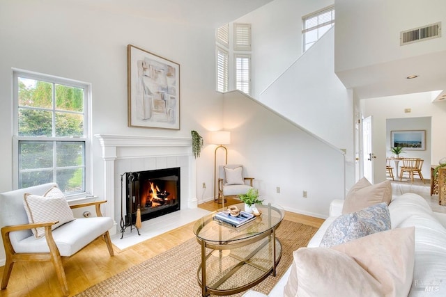 living area featuring a high ceiling, a tiled fireplace, plenty of natural light, wood finished floors, and visible vents