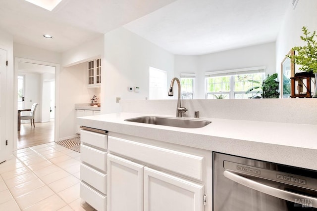 kitchen with dishwasher, a sink, light tile patterned floors, light countertops, and white cabinetry
