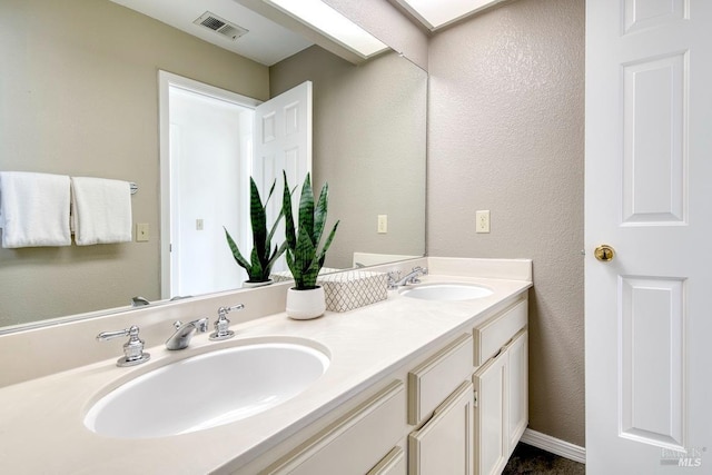 full bathroom featuring visible vents, a sink, a textured wall, and double vanity