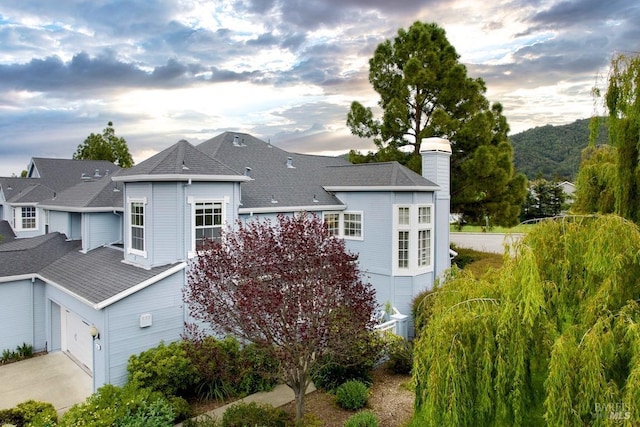 back of property with driveway, a chimney, and a shingled roof