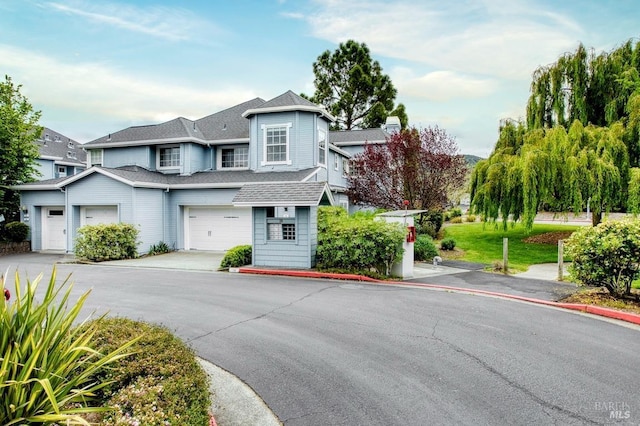 view of front of home with driveway, a shingled roof, and a garage