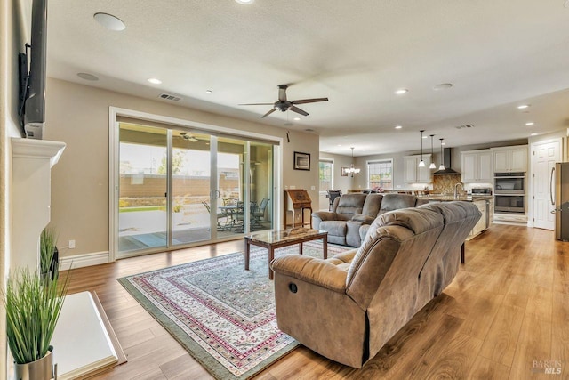 living room featuring light wood-style floors, ceiling fan with notable chandelier, visible vents, recessed lighting, and baseboards