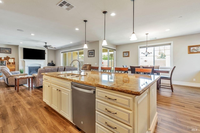 kitchen with visible vents, dishwasher, a sink, cream cabinets, and a glass covered fireplace