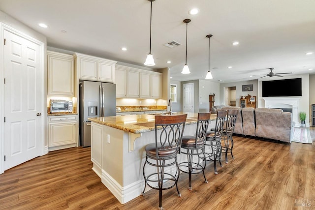 kitchen featuring wood finished floors, ceiling fan, light stone counters, and stainless steel fridge
