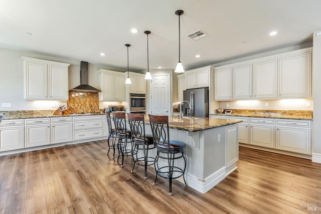 kitchen with light wood-style flooring, visible vents, wall chimney exhaust hood, a kitchen bar, and stainless steel appliances
