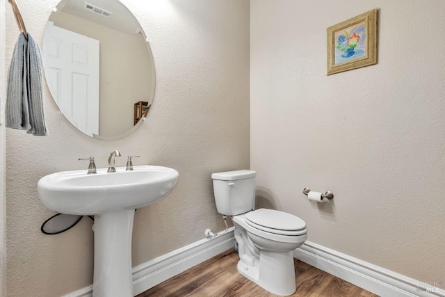 bathroom with toilet, wood finished floors, baseboards, and visible vents