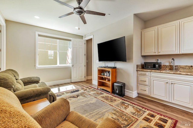 living room featuring light wood-style floors, baseboards, and ceiling fan