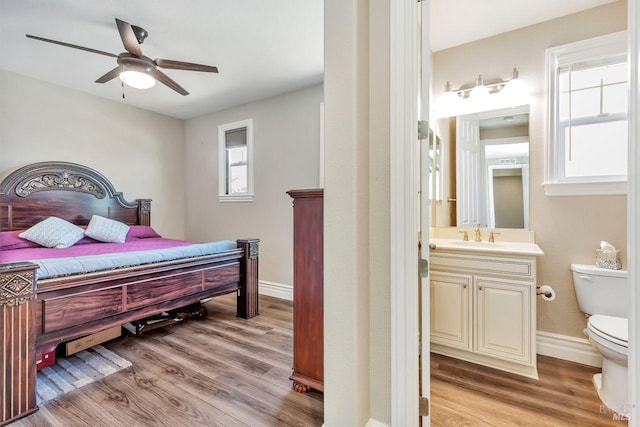 bedroom with light wood-style flooring, baseboards, a sink, and ensuite bathroom